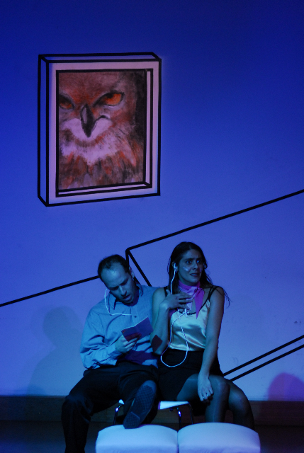 Ein Mann und eine Frau sitzen auf die Bühne. Das Licht ist blau. Hinter ihnen sieht man eine Nahaufnahme eines Eulengesichts.