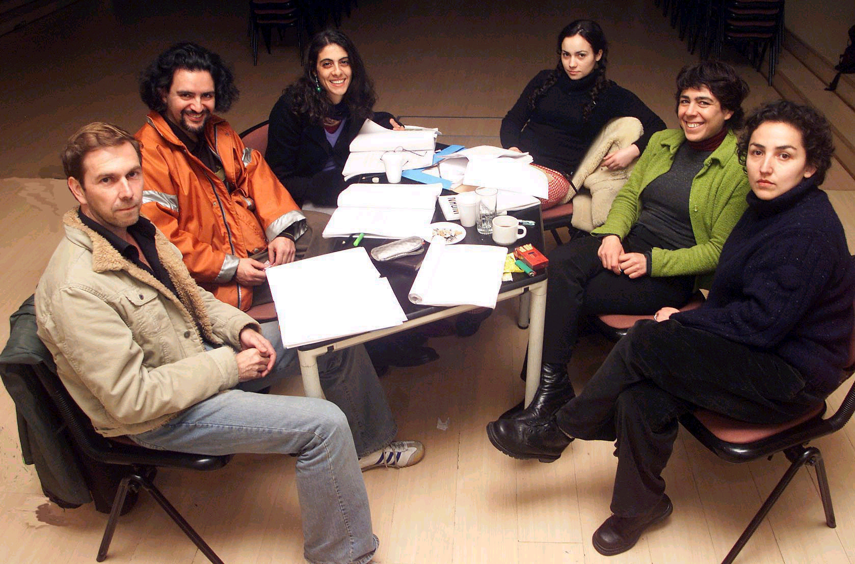 Eine Gruppe von sechs Menschen sitzt an einem Tisch und arbeitet an Theatertexten. Ganz links sitzt René Pollesch.